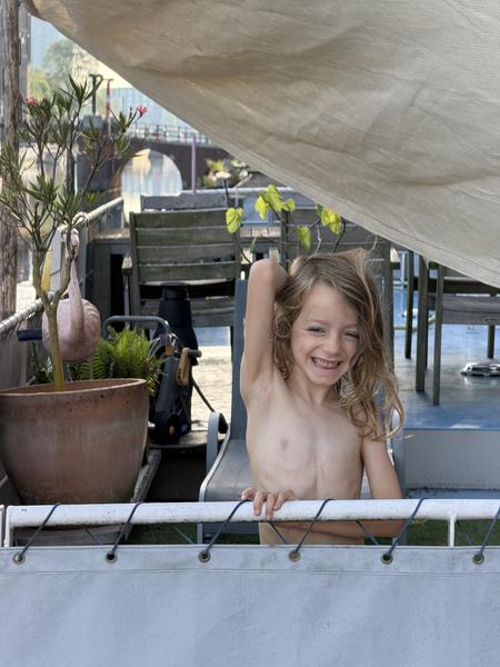 A young child with long hair smiles while posing under a canopy on a patio